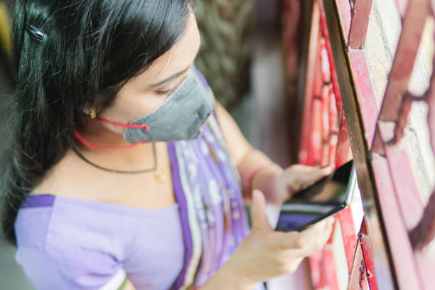 beautiful woman in purple saree and busy with phone. she is standing near window. - multi tasking asian and indian ethnicities asian ethnicity lifestyles imagens e fotografias de stock