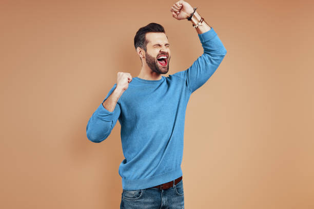 istock Cheerful young man in casual wear shouting and gesturing while standing against brown background 1224569974