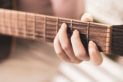 Close up woman playing acoustic guitar at home
