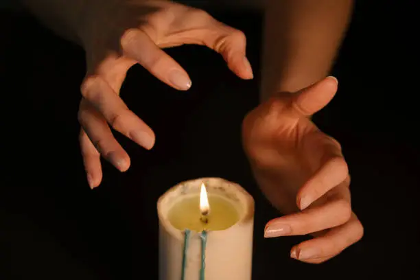 Photo of A clairvoyant witch prediction over a candle. Women's hands over the flame are isolated on a black background. The concept of paranormal, prediction of the future and mysticism