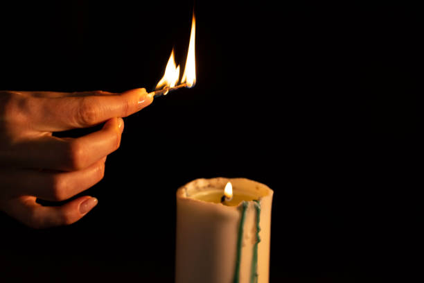 istock Aromatherapy concept - a woman's hand sets fire to a white candle isolated on a black background. Relaxation and meditation in the spa 1224570170