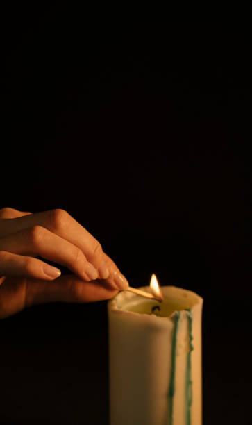 istock A woman's hand sets fire to a candle on a black background with a match. Isolated. The concept of witchcraft, divination and magic 1224570428