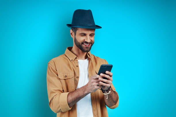 istock Good looking young man smiling and using smartphone while standing against blue background 1224570505