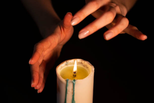 istock Mysterious magic close-up - women's hands conjure over a burning candle in isolation on a black background. The concept of prediction, clairvoyance and divination 1224570746
