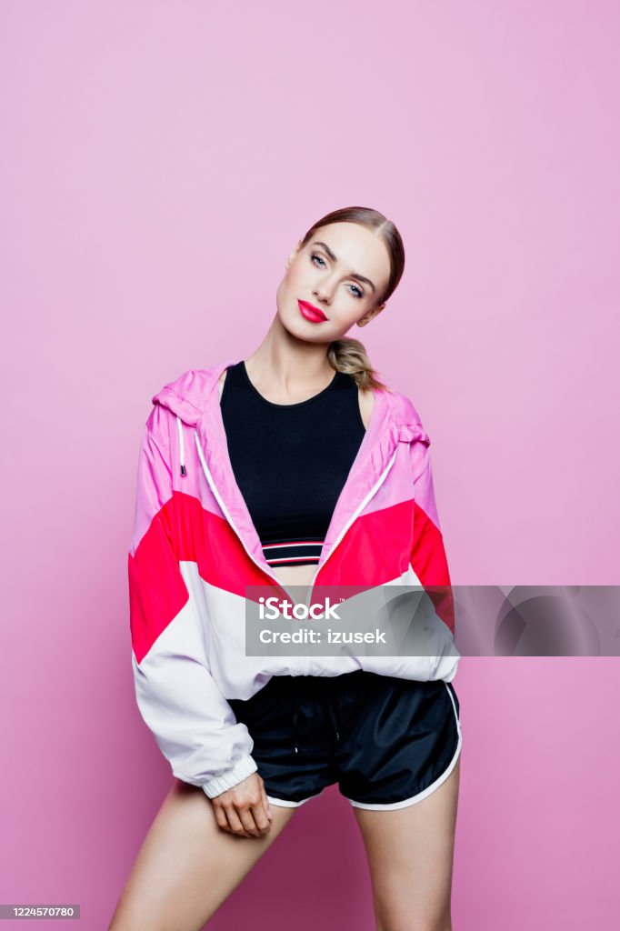 Sport portrait of cheerful woman in tracksuit against pink background Mid adult beautiful woman wearing oversized tracksuit and black shorts and top standing against pink background, smiling at camera. Fashion Model Stock Photo
