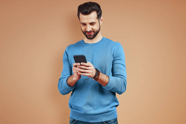 istock Smiling young man in casual wear using digital tablet while standing against brown background 1224572252