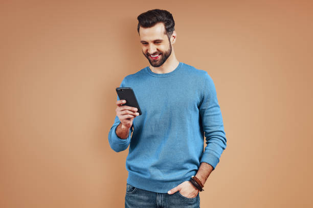 istock Handsome young man in casual wear using digital tablet while standing against brown background 1224573646