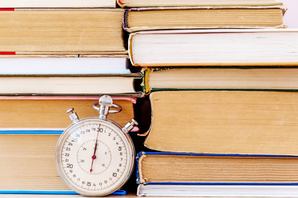 Stack of books and stopwatch on simple backdrop. Copy space for your text.