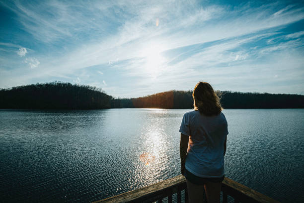 girl looking out alone over the water - water lake reflection tranquil scene imagens e fotografias de stock