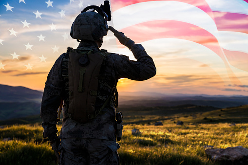 Silueta de un solider saludando contra la bandera de EE.UU. en el amanecer photo