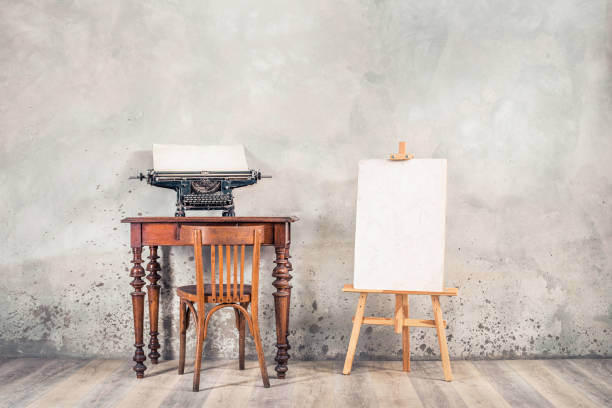 Vintage typewriter with sheet of paper on old oak desk, easel, painting canvas blank, aged chair front grunge concrete wall background. Artist's classic workplace concept. Retro style filtered photo máquina de escribir vintage con hoja de papel en el escritorio de roble viejo, caballete, pintura de lienzo en blanco, silla envejecida fondo de pared de hormigón grunge frontal. concepto de lugar de trabajo clásico del artista. foto filtrada de estilo