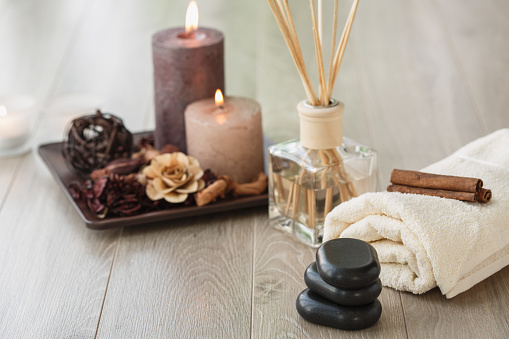 Copyspace of wooden floor in a spa center where different tools are ready for a relaxing session of massage and mindfulness. Volcanic stones, towel, candles and aroma diffuser are visible.