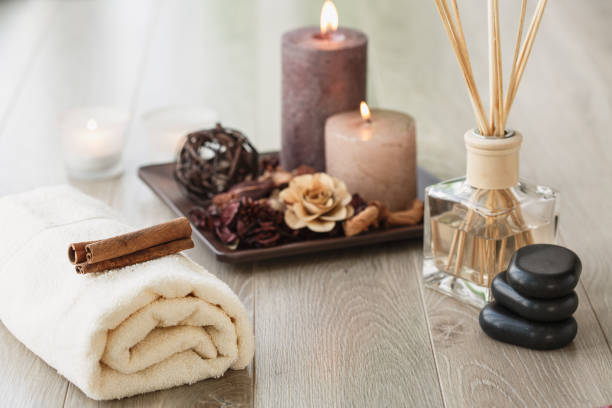 High angle view of wooden floor in a spa center where different tools are ready for a relaxing session of massage and mindfulness. Volcanic stones, towel, candles and aroma diffuser are visible.