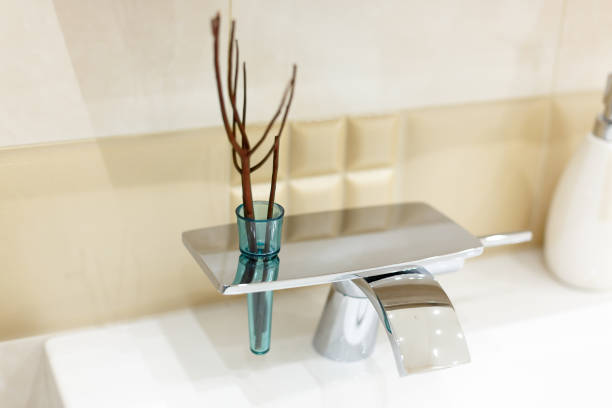 Detail of a white rectangular designer kitchen sink with chrome water tap against a tiled wall