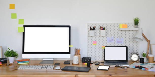 흰색 거실 벽에 그래픽 디자이너 장비로 둘러싸인 나무 작업 책상에 흰색 빈 화면이있는 컴퓨터 노트북 및 컴퓨터 모니터의 사진. - messy adhesive note office computer 뉴스 사진 이미지
