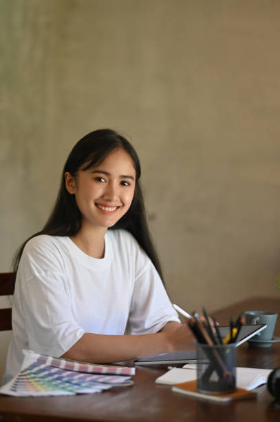 istock Photo of costume designer woman sketching on computer tablet by using a stylus pen while sitting at the wooden working desk over comfortable office cement wall as background. 1224586984