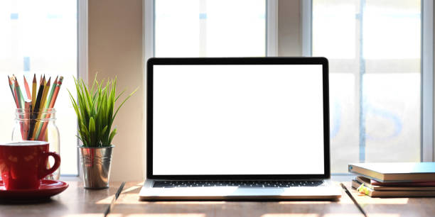 istock Computer laptop with white blank screen putting on wooden working desk that surrounded by coffee cup, stack of books, potted plant, pencils over comfortable living room windows as background. 1224587828