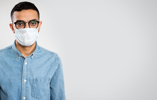 Coronavirus. Serious Arab young man in medical mask on a gray background with space for text and slogan \