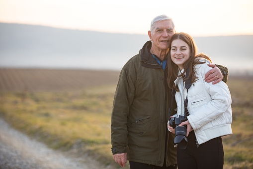 Portrait of Grandfather Embracing Granddaughter Outdoors in Rural Scene.