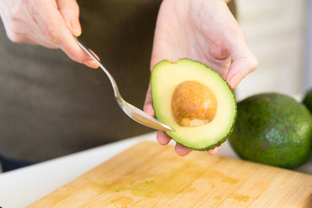 istock Hands of woman removing core from avocado with spoon 1224590725