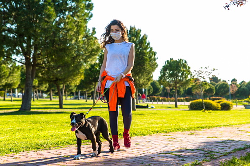 Woman With A Face Mask Walking Her Dog In Park.