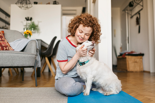 Happy young woman with red curly hair hugging and cuddling her pet dog, relaxing and having fun