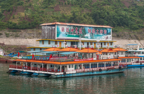 Xinling, China - May 6, 2010: Xiling gorge on Yangtze River. Local short river cruise ofice building termina and boatsl on green water. Green mountain slope as backdrop. Colorful billboard.