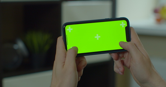 Young man holding smartphone in hands, playing mobile game. Mobile telephone with green screen in chroma key