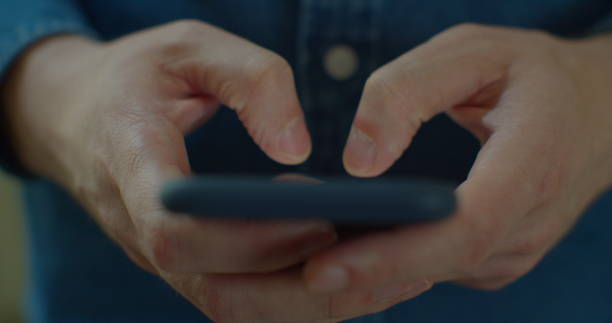 istock Young man holding a smartphone in hands and typing on screen while chatting in the living room at home. Indoors. Close-up. 1224596677