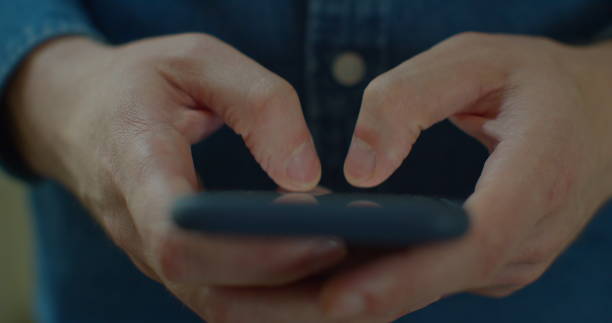 istock Young man holding a smartphone in hands and typing on screen while chatting in the living room at home. Indoors. Close-up. 1224596698