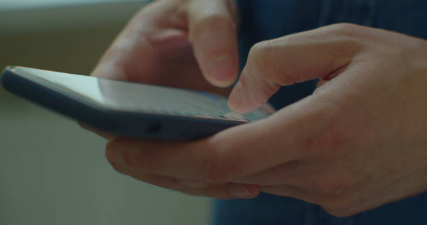 istock Young man holding a smartphone in hands and typing on screen while chatting in the living room at home. Indoors. Close-up. 1224596710