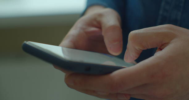 istock Young man holding a smartphone in hands and typing on screen while chatting in the living room at home. Indoors. Close-up. 1224596729