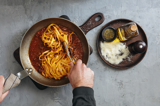 Man Cooking Classic Tagliatelle with Sauce Bolognese. Flat lay top-down composition on concrete background