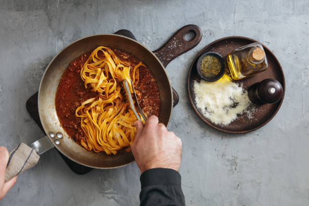 Man Cooking Classic Tagliatelle with Sauce Bolognese Man Cooking Classic Tagliatelle with Sauce Bolognese. Flat lay top-down composition on concrete background cooking pan overhead stock pictures, royalty-free photos & images