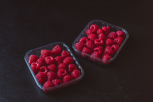 Fresh raspberries in plastic container on dark background.