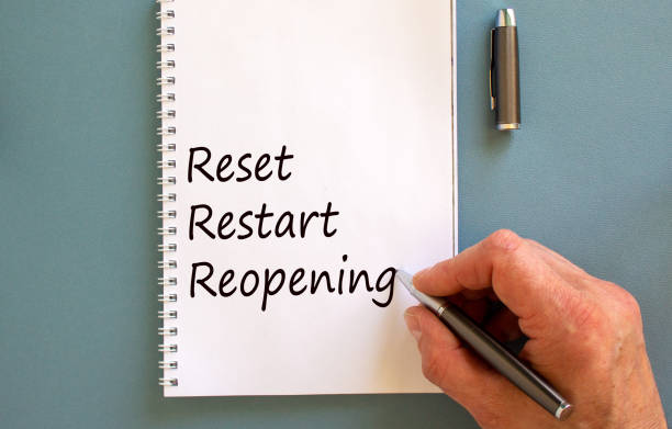 istock Male hand writing 'reset, restart, reopening' on white note, isolated on blue background. 1224610060