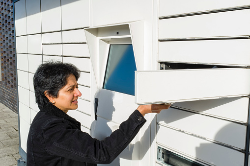 British Asian woman using an automated postal locker, parcel collection point in UK