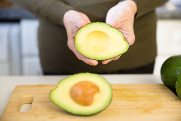 istock Woman showing avocado cut half over kitchen table 1224614647