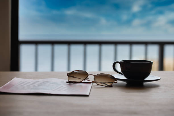 Romantic Breakfast in a Cafe on the Beach. White Coffee Cup on the Wooden Beach Table. cofee with sunglasses and news paper. beach background. holiday background. restaurant open. cafe coffee background