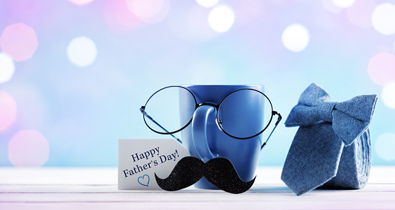 Celebration background on Happy Father day. Creative breakfast with funny face from cup of coffee, eyeglasses and mustache. Greeting card for daddy with copy space and bokeh.