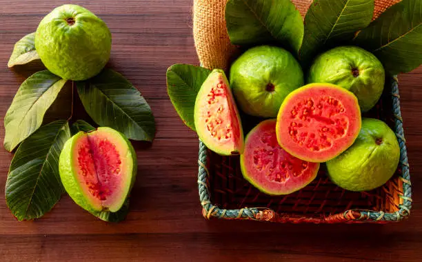 Fresh red guavas with green leaves on wooden demolition background. Wood texture and guava leaves