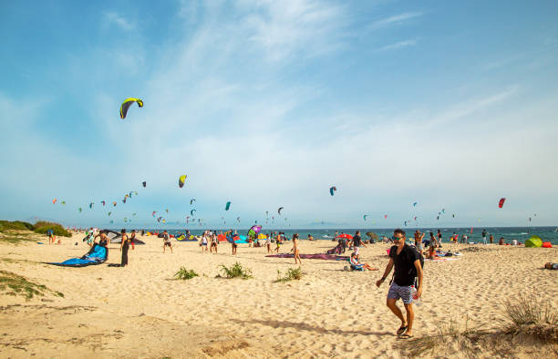TARIFA, SPAINE - July 19, 2018: Beautiful white Tarifa beach packed with kitesurfers and sunbathers. One of the best places to practice kitesurfing TARIFA, SPAINE - July 19, 2018: Beautiful white Tarifa beach packed with kitesurfers and sunbathers. One of the best places to practice kitesurfing"n"n"n"n kiteboarding stock pictures, royalty-free photos & images
