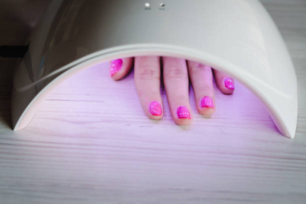 istock Woman hand inside lamp for nails on table close up. UV lamp with light for drying nails with gel polish. violet nails dried in the lamp. Girl makes a manicure at home, doing manicure herself, draws. 1224638170
