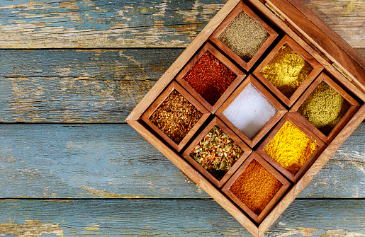 Different bright herbs indian spices in wooden boxes on old wooden background
