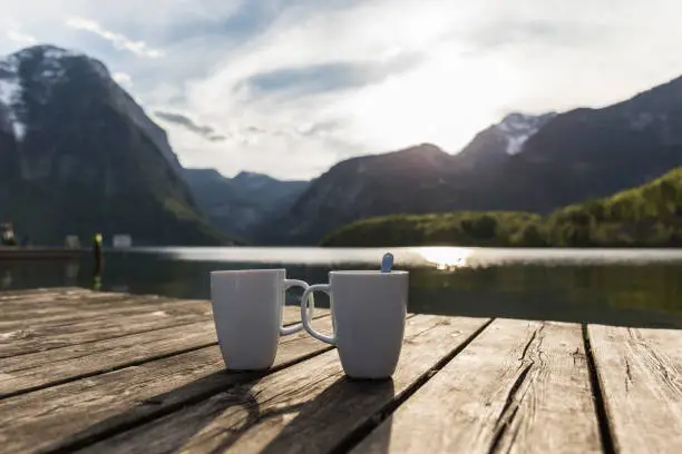 two white cups on a wooden platform next to a lake between mountains in Austria at sunset