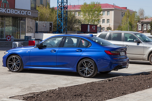 Novosibirsk, Russia - 04.26.2020: The new BMW 3 series car of a bright blue shiny metallic color against the backdrop of an urban Russian landscape. German expensive car in the stone jungle.