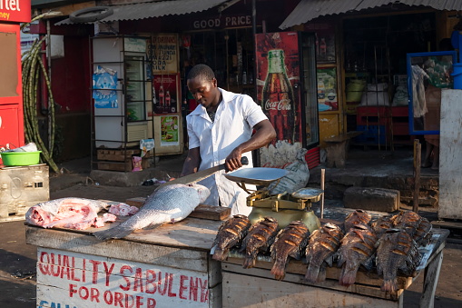 Kampala, Uganda - January 12th, 2020: Unidentified vendor cuts a Nile perch at a street market in Kampala, Uganda. The Lake Victoria is known for the rich catch of Nile perch and Tilapia fishes.