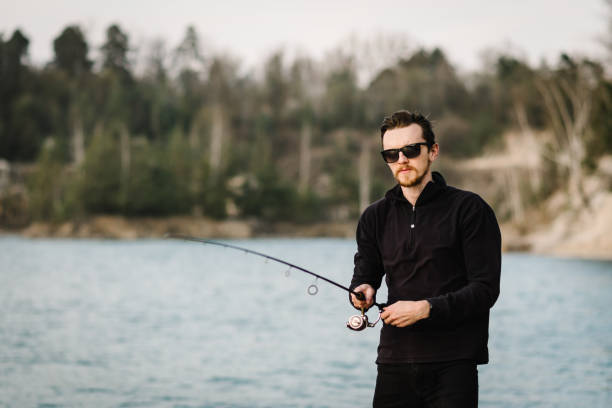 istock Fisherman with rod, spinning reel on the river bank. Man catching fish, pulling rod while fishing from lake or pond with text space at weekend. Fishing for pike, perch, carp on beach lake or pond. 1224641639