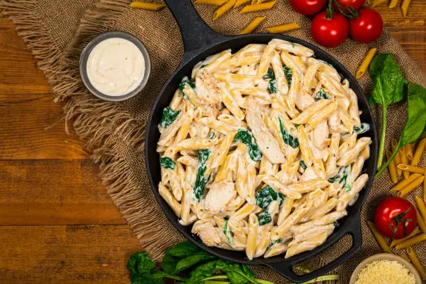 Chicken Alfredo Parmesan Penne Pasta with Spinach on Wooden Background Top View. Selective focus.