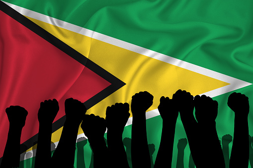 Silhouette of raised arms and clenched fists on the background of the flag of GUYANA. The concept of power,  conflict. With place for your text. 3D rendering